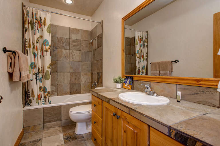 Refresh and recharge in your private bathroom, featuring natural stone tiling, a deep soaking tub, and warm wood accents that create a cozy retreat after a day of mountain adventures.