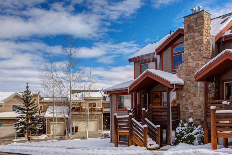 Cozy mountain retreat nestled in a snowy neighborhood with charming stone chimney, wooden deck, and alpine surroundings—perfect for your winter getaway.