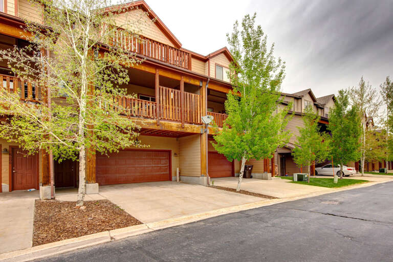 A mountain-style residential property featuring warm wood siding, expansive balconies, and mature aspen trees. The building is located within a well-maintained neighborhood with accessible parking and scenic surroundings.