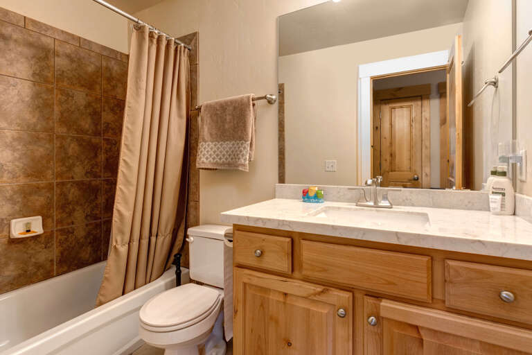 Step into your private bathroom featuring a spacious tub-shower combo, marble countertops, and warm wood cabinetry. Soft towels and toiletries await to make your stay comfortable and relaxing.