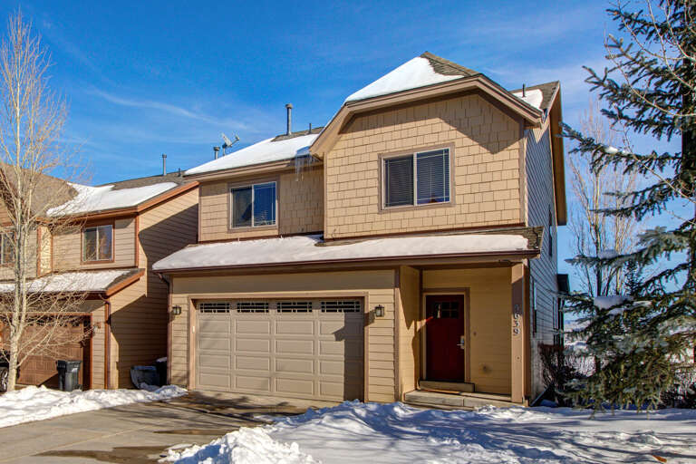Snow-dusted exterior of a welcoming mountain home nestled among evergreens, offering comfortable vacation living with convenient garage parking in a peaceful residential setting.