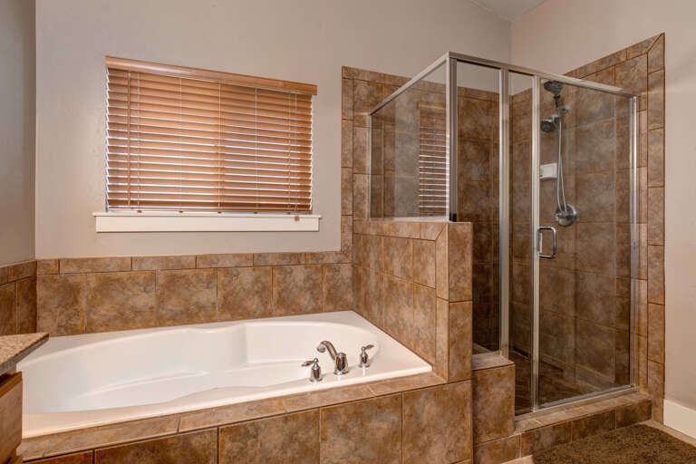 Soak in the spacious soaking tub or refresh in your private walk-in shower, beautifully finished with warm natural stone tile and soft natural light from the window.