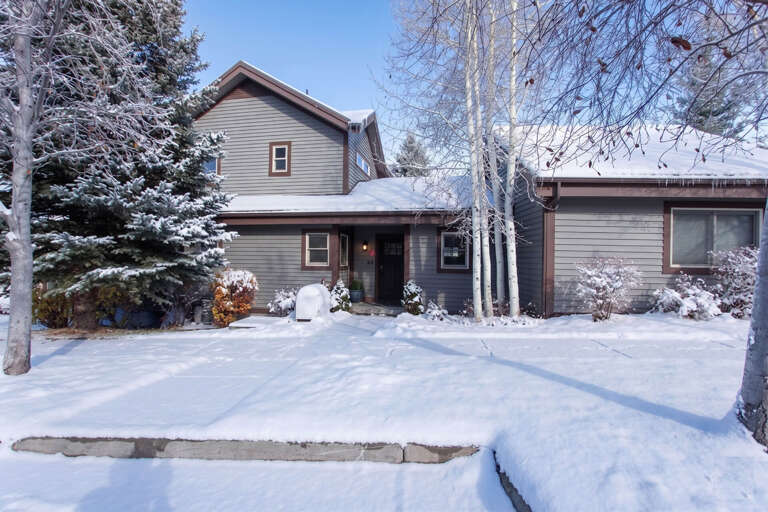 This inviting property nestled among snow-dusted evergreens and bare winter birches provides a serene mountain retreat with ample parking and a welcoming entrance.