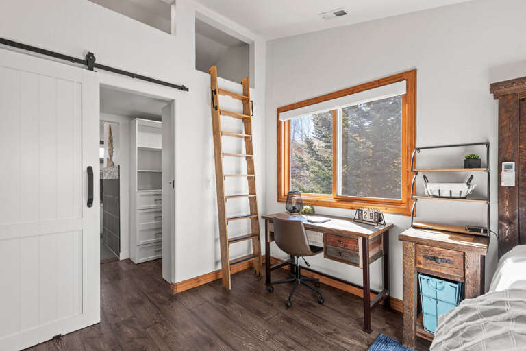 Bright workspace with natural views and mountain scenery framed by warm wood tones, complete with a cozy loft above and sliding barn door for privacy.