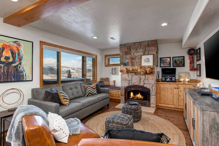 Settle into your cozy living room where a crackling stone fireplace sets the mood. Mountain views frame your relaxation, and rustic wood details add warmth to every moment you unwind here.