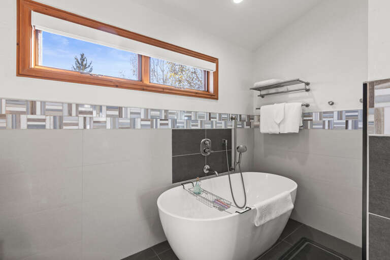 Slip into a luxurious soak in your modern freestanding tub, framed by natural light from high windows and surrounded by sleek, contemporary tile work and fresh towels ready for you.
