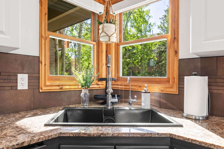 Prepare meals surrounded by natural light streaming through stunning corner windows overlooking lush greenery. This modern kitchen blends rustic wood with sleek finishes for your perfect getaway.