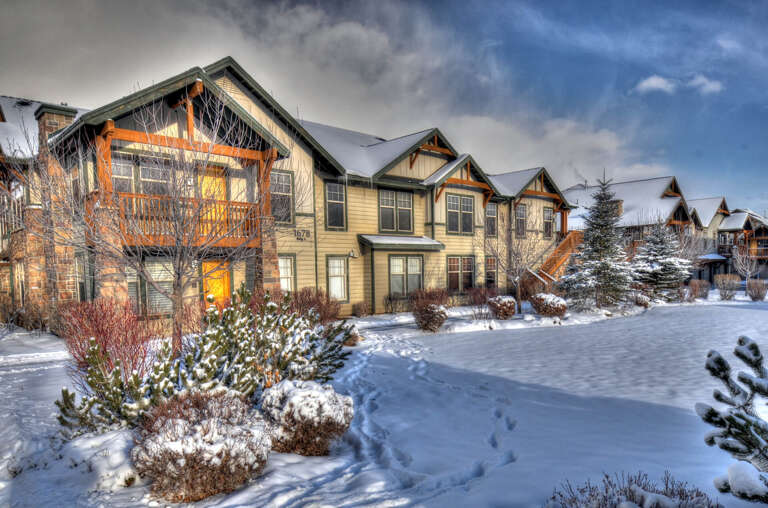 A row of cozy mountain-style townhomes set against snowy landscaping and a dramatic winter sky, capturing the property's seasonal charm and alpine setting.