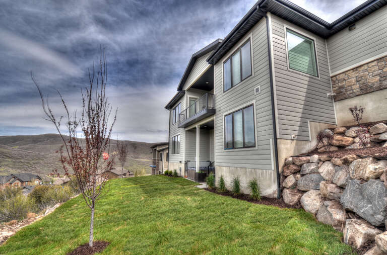 Modern two-story home featuring stone and siding exterior, situated on a landscaped hillside with mountain backdrop and neighboring community views.