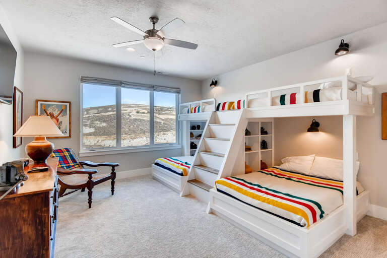 This cheerful bedroom features custom bunk beds with vibrant striped bedding, vintage furnishings, and stunning desert views through expansive windows.