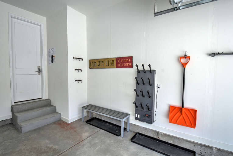 A bright, organized mudroom or garage entry with bench seating, wall hooks, and an orange snow shovel—ready to help you settle in or gear up for outdoor adventures.