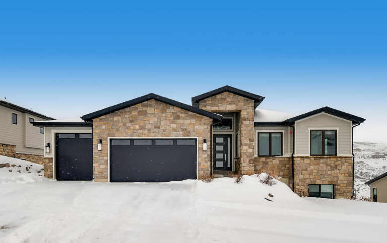 A modern stone and stucco home set against a serene winter landscape, offering proximity to mountain views and scenic surroundings during the snowy season.