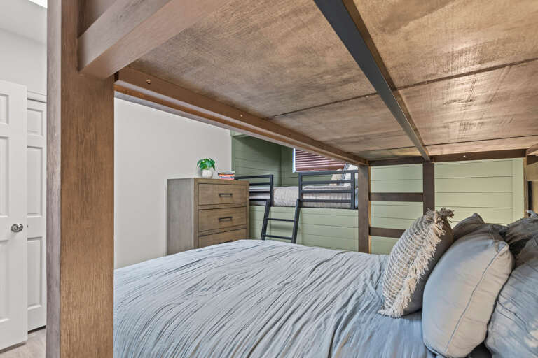 Unwind in your cozy bedroom featuring a plush queen bed, custom wood-beam canopy ceiling, and a charming bunk area—perfect for families or groups seeking rustic comfort with modern style.