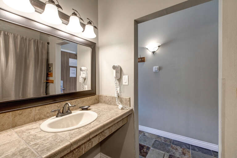 Beige-themed sink area with mirror and overhead lights. Beige-themed sink area with mirror and overhead lights.