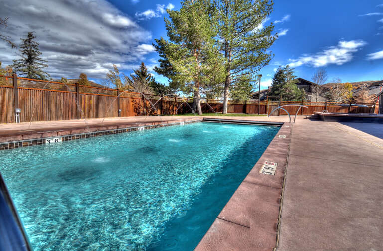 A private fenced pool area surrounded by mature pines and stunning mountain views, perfect for refreshing dips under wide-open skies.