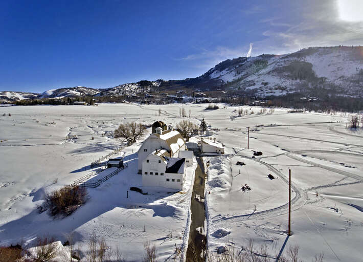 Aerial view of a charming property nestled in a pristine winter valley, surrounded by snow-covered mountains and peaceful countryside.