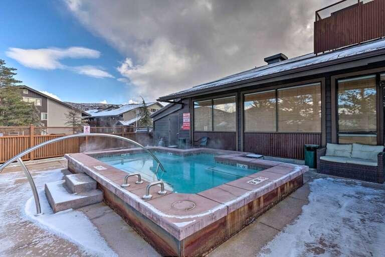 A spacious hot tub awaits under open skies, surrounded by snow-dusted mountains and modern buildings—perfect for relaxing after a winter day outdoors.