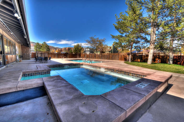 The property features a refreshing outdoor pool with a hot tub, surrounded by mature trees and a peaceful mountain backdrop—perfect for sunny days.