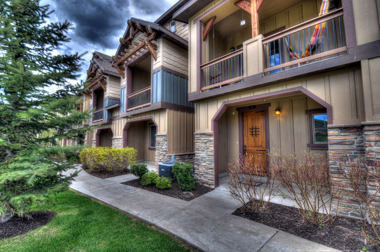 Mountain retreat architecture blends natural stone and timber details, with private balconies overlooking a lush, landscaped courtyard lined with evergreens.