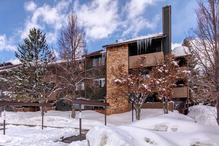 A charming mountain retreat nestled among pines and aspens, with snow-draped balconies and icicles glistening in the winter sun—your perfect alpine getaway awaits.