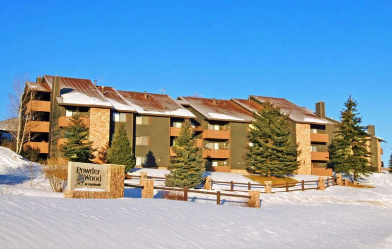 Powderwood at Sunbrook property sits nestled among snow-covered pines on a crisp winter day, its rustic alpine architecture welcoming guests to a mountain retreat.