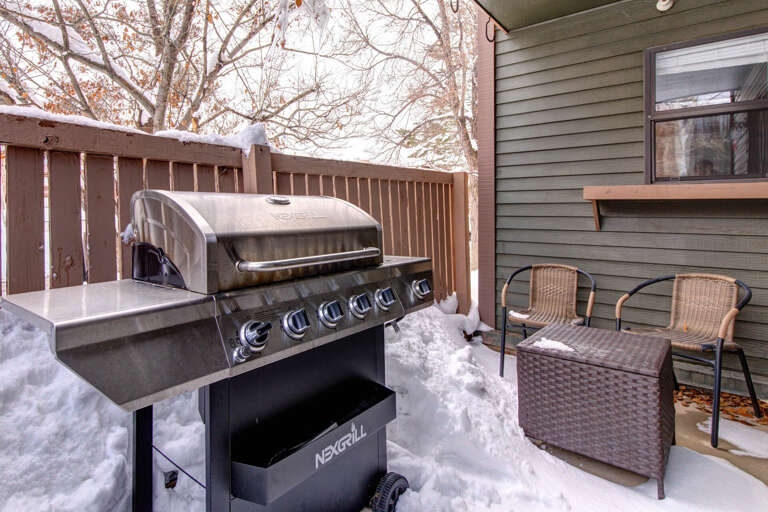 A private outdoor patio features a full-sized gas grill and cozy seating surrounded by winter scenery—perfect for those who love seasonal charm and fresh mountain air.