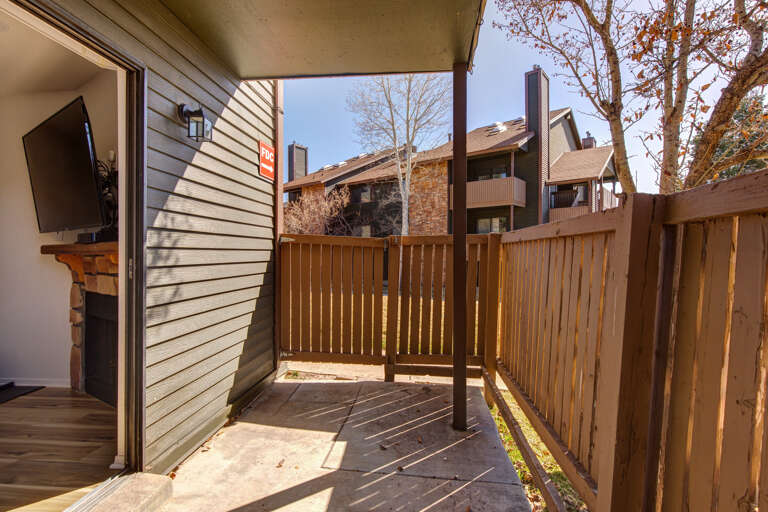 A private patio offers a peaceful spot to enjoy your morning coffee, with autumn trees and neighboring buildings visible beyond the wooden fence.
