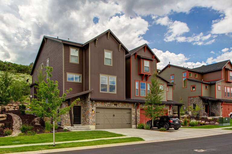 Modern townhome nestled in a scenic mountain neighborhood, featuring stone accents and private garage parking amid landscaped surroundings.