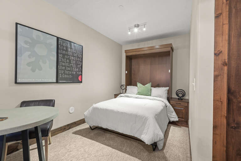 Your cozy retreat features plush bedding with crisp linens and a splash of color, all tucked beneath modern track lighting. The space-saving Murphy bed design maximizes your room while keeping it warm and inviting.