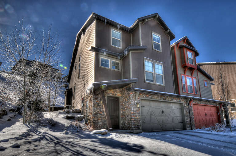 Modern mountain townhome nestled in a snowy neighborhood, combining contemporary design with natural stone accents and convenient garage access.