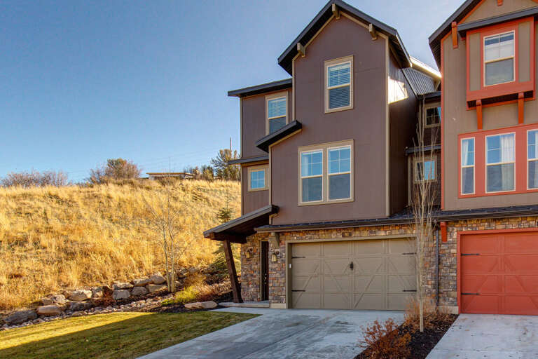 Modern townhome exterior nestled against natural hillside terrain in a quiet residential neighborhood, offering convenient access to outdoor recreation and mountain living.
