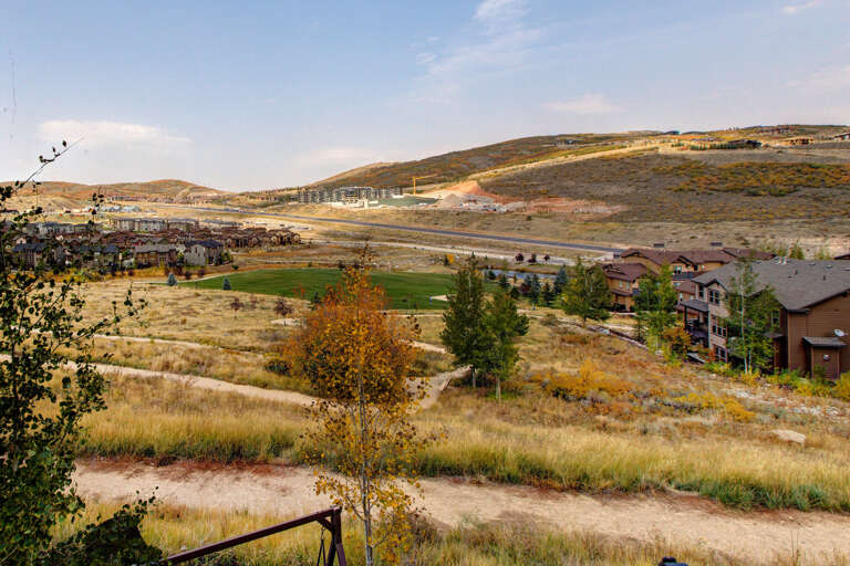A scenic hillside development nestled among rolling terrain with residential buildings, autumn foliage, and open green spaces throughout the valley.