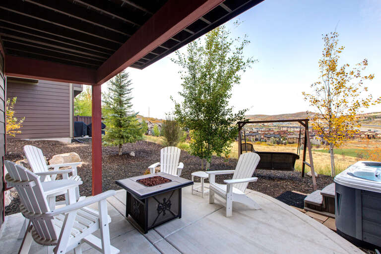 Covered patio with fire pit and hot tub overlooking scenic valley views and distant hills, perfect for peaceful evenings under the open sky.