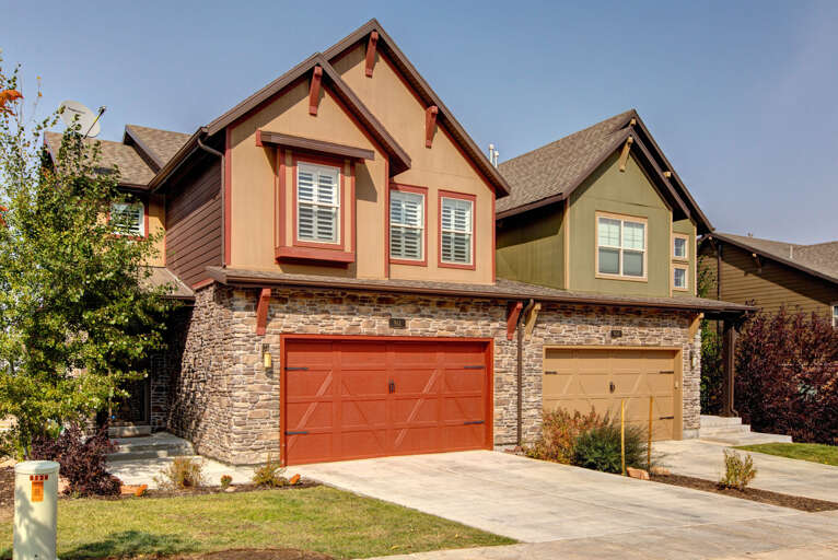 Charming multi-unit property featuring distinctive architectural details with stone accents, individual garages, and a welcoming residential setting surrounded by mature landscaping.