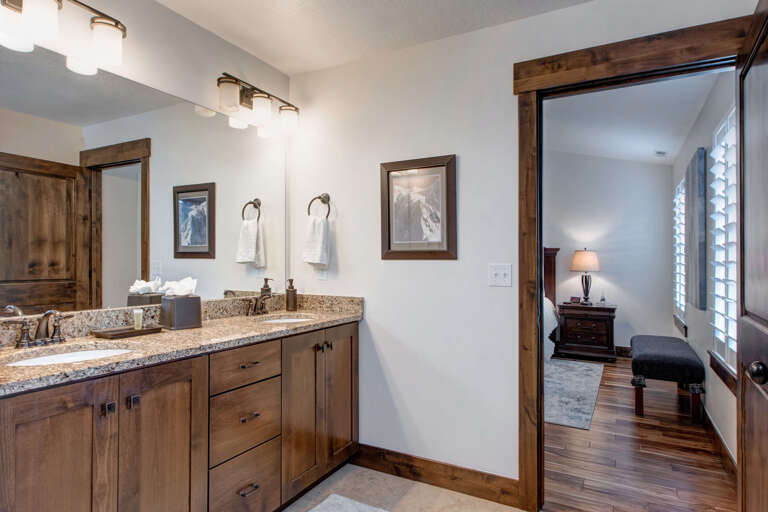 Your private bathroom features warm wood cabinetry, granite countertops, and crisp white towels, with direct access to your cozy bedroom just steps away.