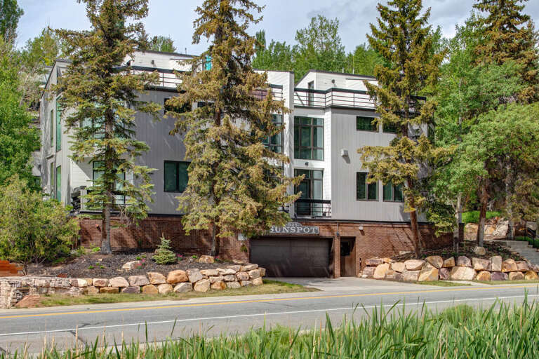 A contemporary mountain property nestled among mature pines, featuring modern architecture with brick accents and natural stone landscaping integrated into the surrounding forested hillside.