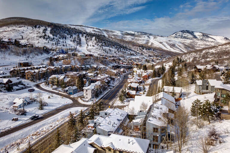 A picturesque mountain resort town nestled in a snow-covered valley, surrounded by ski slopes and alpine peaks under a clear blue winter sky.