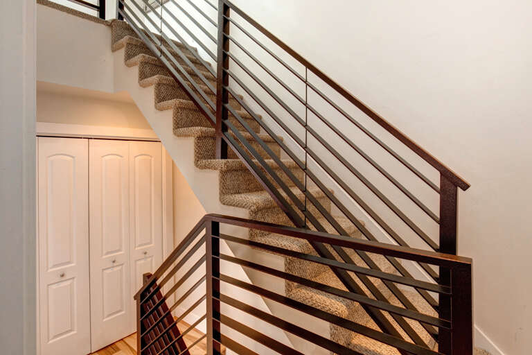 A modern carpeted staircase with sleek metal railing and convenient under-stair storage completes this multi-level home design.