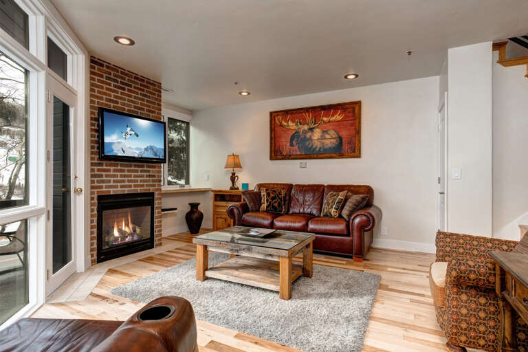 Cozy up by the fireplace in your inviting living room, where rustic charm meets modern comfort with warm wood floors, rich leather seating, and a TV for your entertainment.