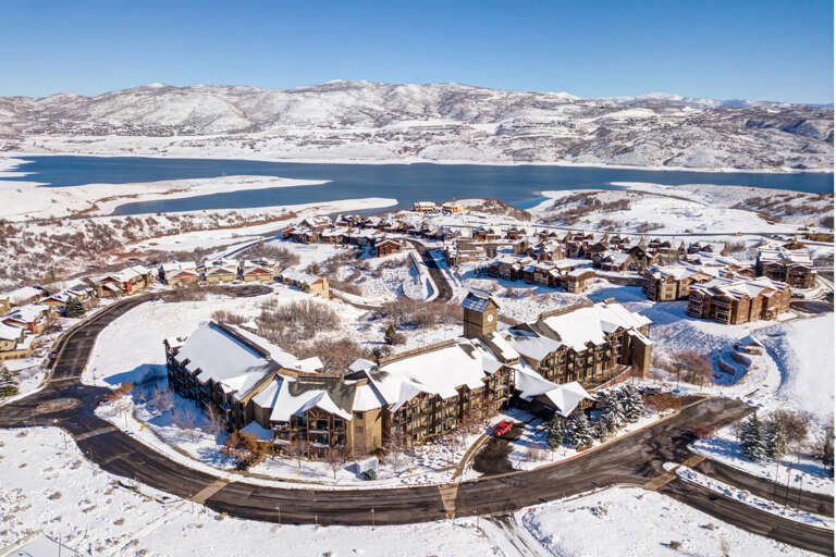 Aerial view of a lakeside resort community nestled in snow-covered mountains, showcasing the property's stunning winter setting and scenic surroundings.