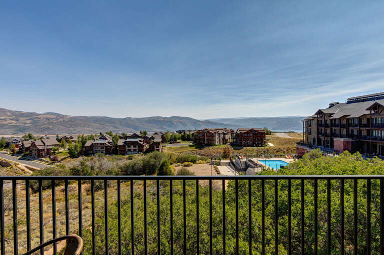 Scenic mountain and lake views stretch across a hillside community with a sparkling pool below, framed by clear blue skies and rolling hills.
