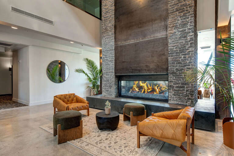 A soaring double-height lobby welcomes you with warm leather seating, tropical greenery, and a dramatic modern fireplace framed by natural stone—designed for stylish comfort from the moment you arrive.