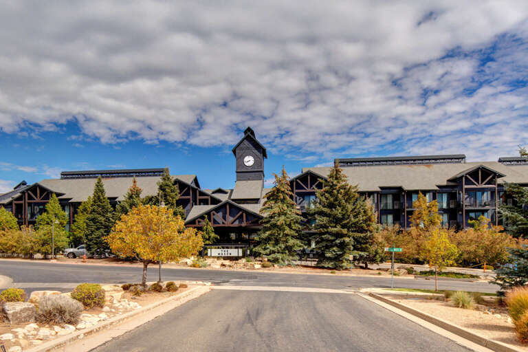 Distinctive mountain resort architecture features rustic timber framing and a prominent clock tower, surrounded by landscaped grounds and seasonal foliage marking the entrance to the property.