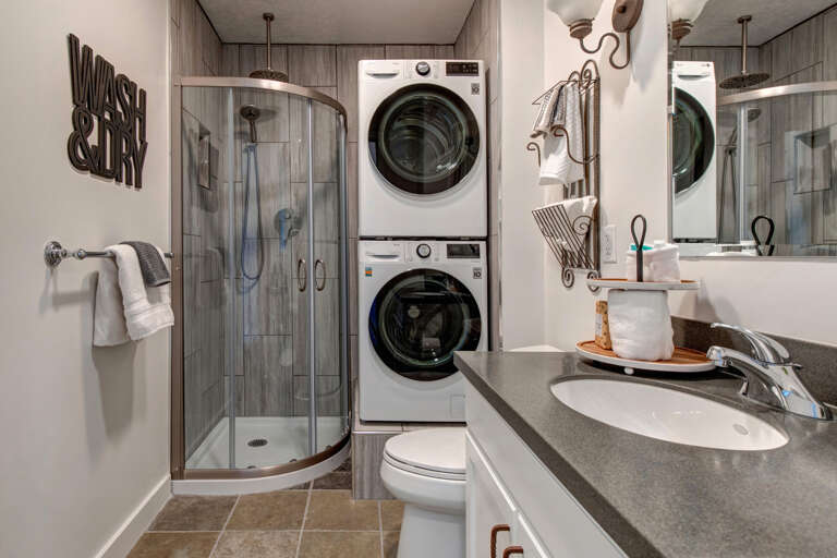 Step into your beautifully designed bathroom with everything you need—stacked washer and dryer, curved shower enclosure, and modern countertop vanity—thoughtfully arranged for your comfort and convenience during your stay.