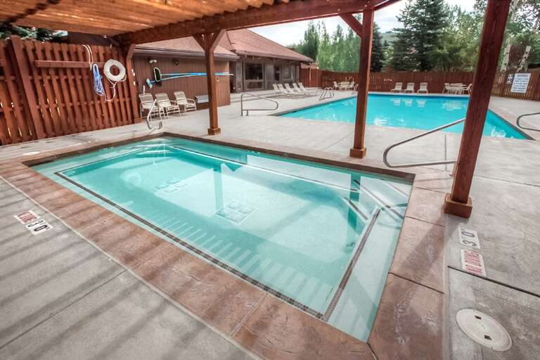 Two inviting pools await—one shallow for a soothing soak, one larger for leisurely swims—both framed by warm wood pergolas and mountain-backed views.