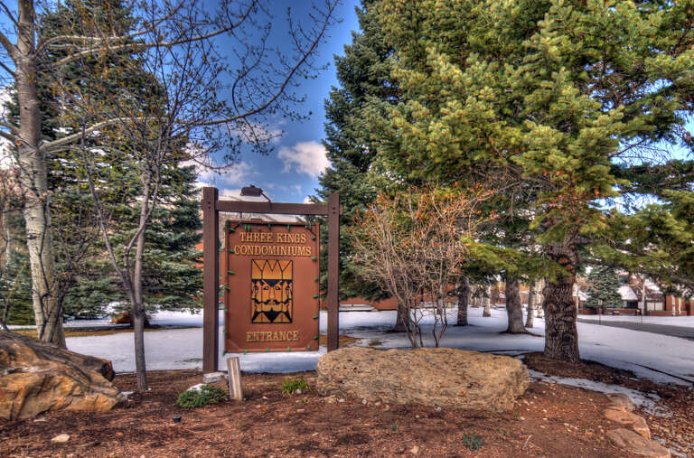 The Three Kings Condominiums entrance sign stands amid evergreens and snow, marking the property's location in a scenic mountain setting.