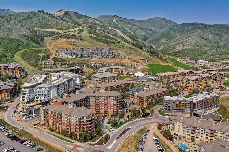 Mountain resort village nestled among rolling green peaks with ski runs visible on the hillsides, surrounded by summer landscapes and natural terrain.
