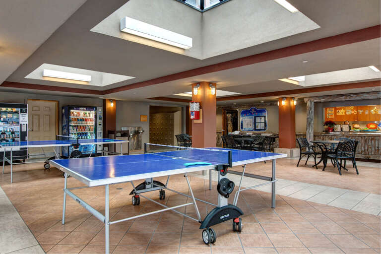 Bright communal recreation area features table tennis and vending refreshments beneath natural skylights, with comfortable seating and an inviting breakfast station nearby.