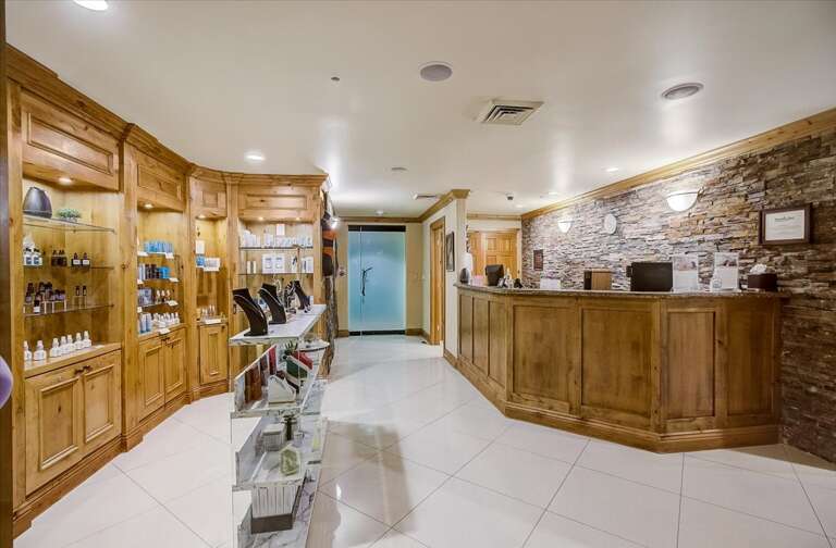 A welcoming lobby area featuring a custom wooden reception desk set against rustic stone accents. Browse curated retail displays in handcrafted wood cabinetry while you check in to start your getaway.