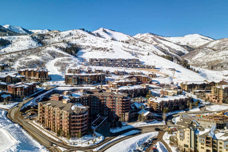 Aerial view of a ski resort village nestled in snow-covered mountains, with ski slopes, lifts, and surrounding residential buildings.